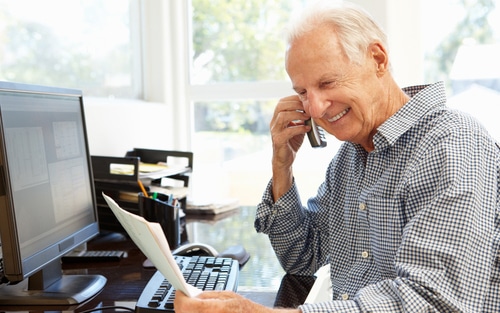 older man on the phone smiling while looking down at his paper